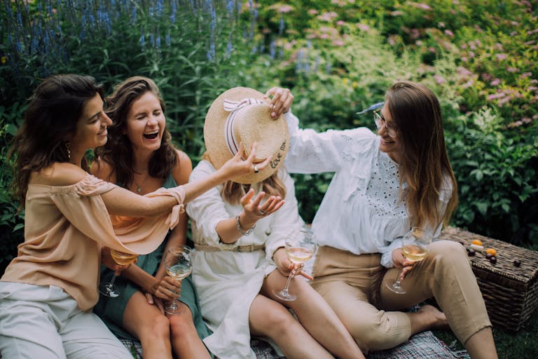 Four women enjoying a fun, relaxing picnic, sharing wine in a lush garden setting.