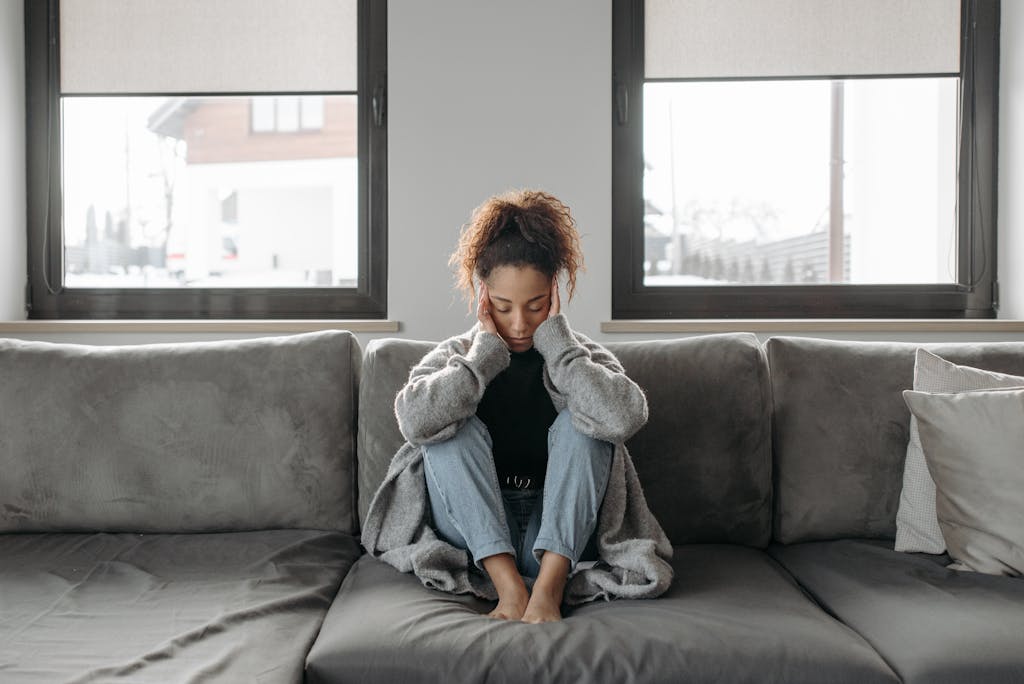 A woman sits on a sofa looking unwell, emphasizing a sense of illness or fatigue indoors.
